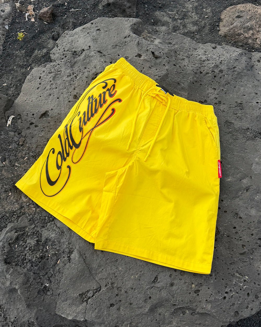 SCRIPT SWIMSHORTS YELLOW - yellow script print swim shorts, flat lay - Cold Culture